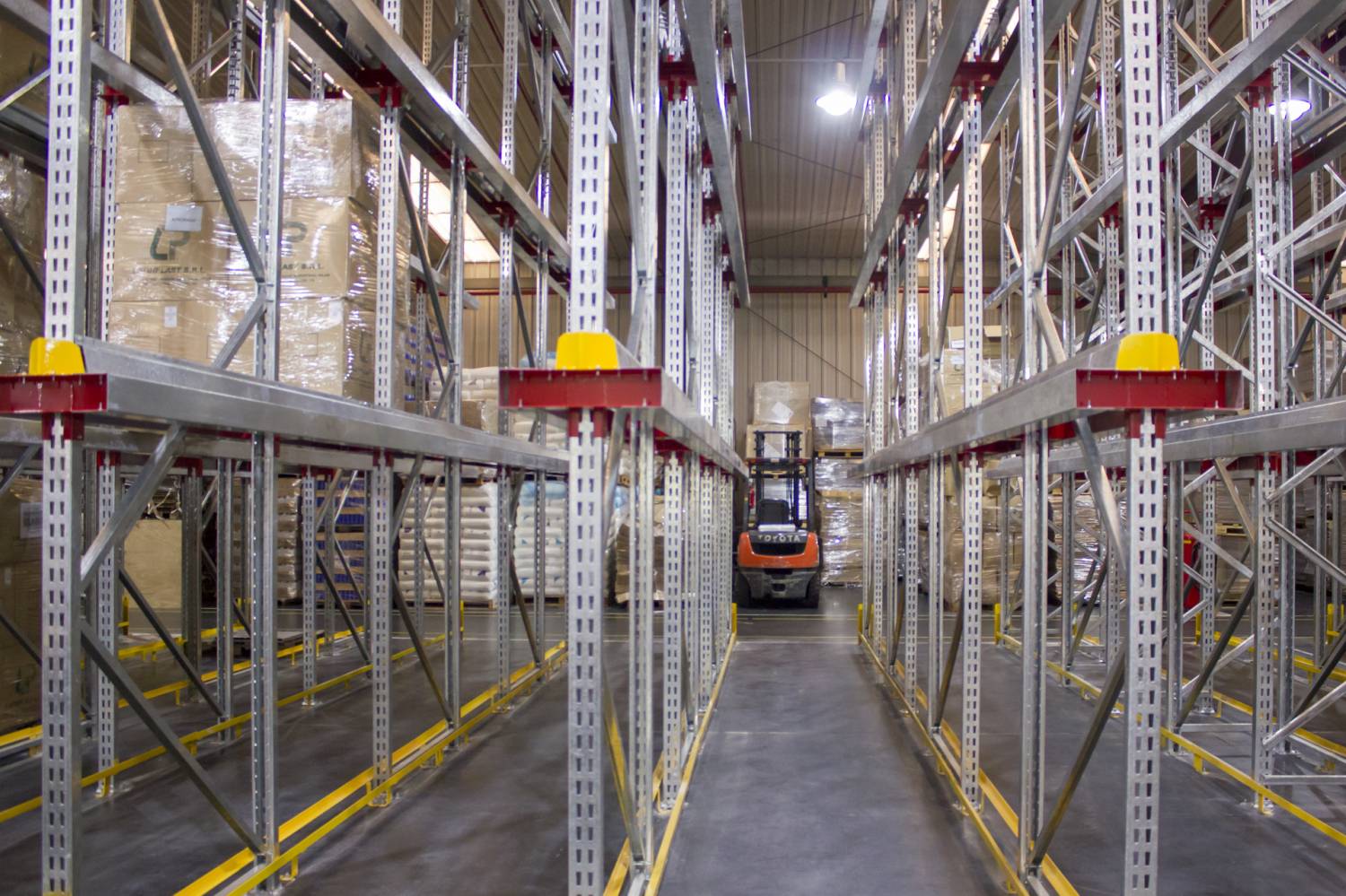 Pasillo interior de rack Drive-In con autoelevador operando en depósito de empresa plástica.