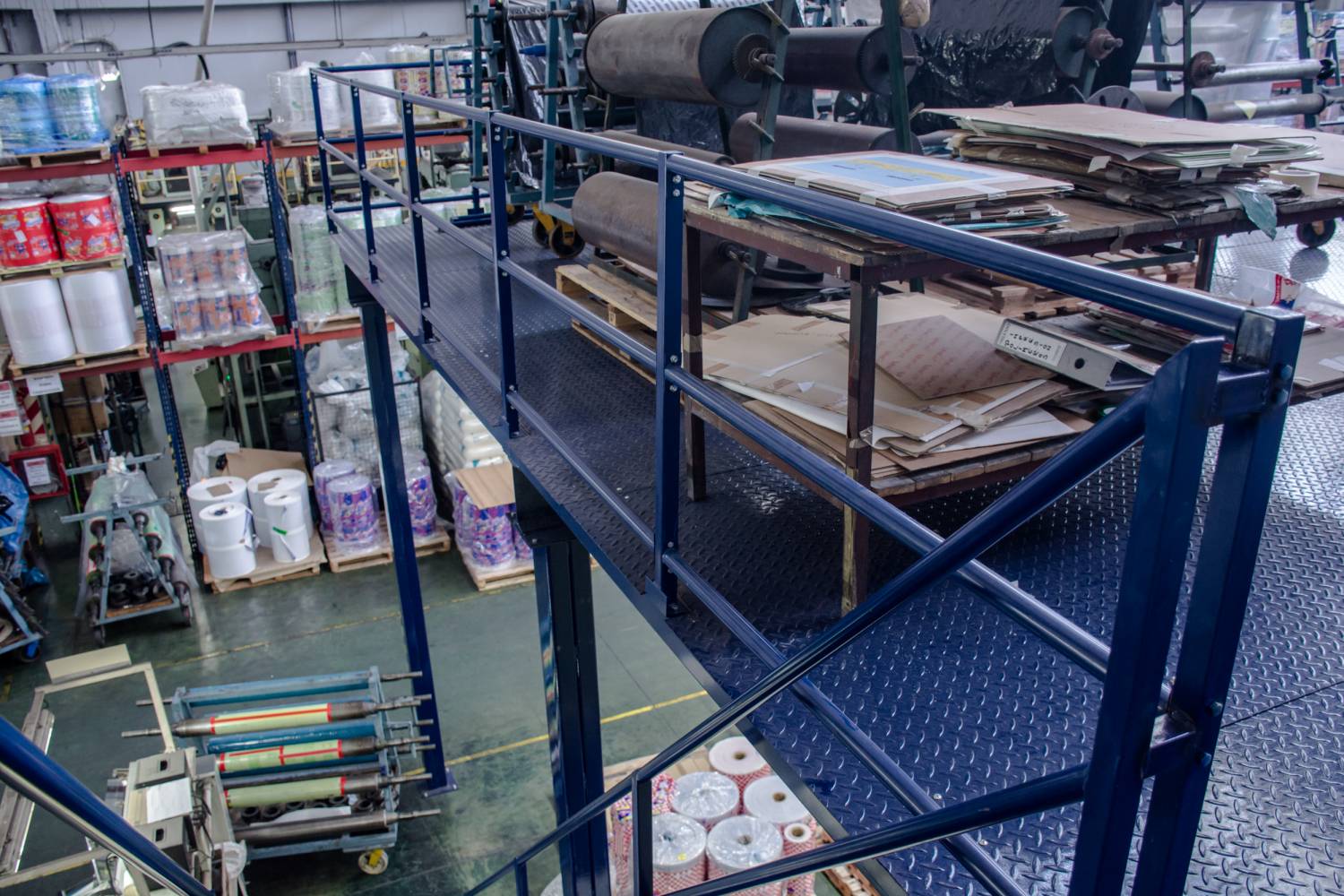 Nivel superior del entrepiso normalizado con materiales gráficos almacenados y barandas de seguridad.